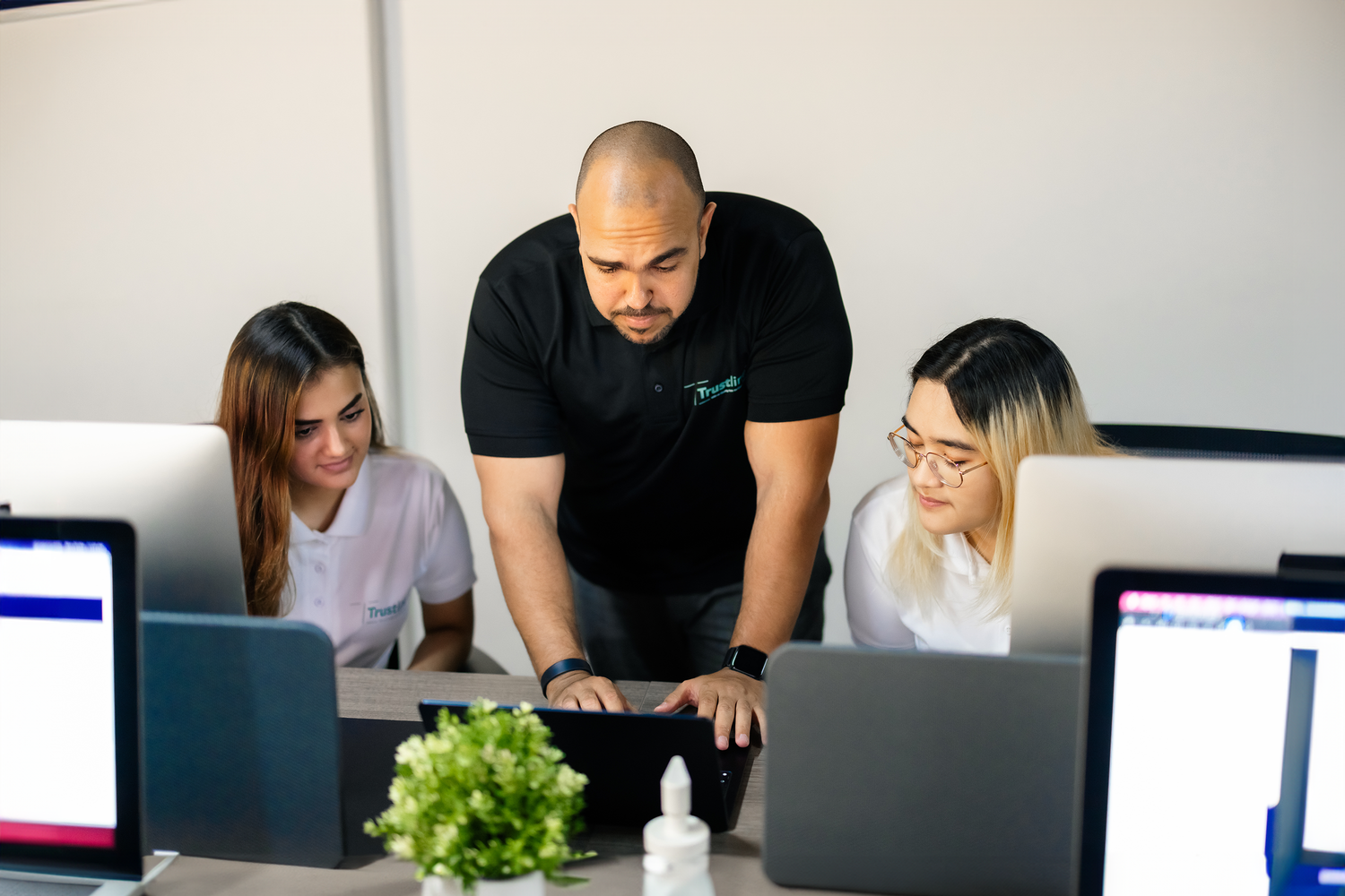 A team leader guiding two employees on their laptops.