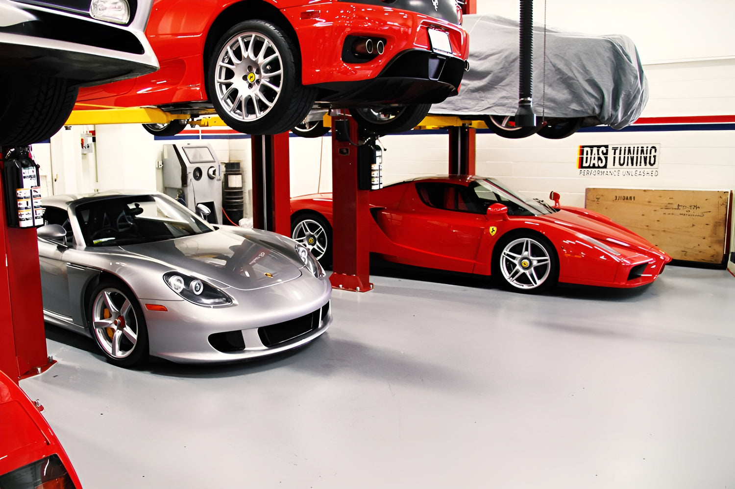 Interior of a high-end car tuning and performance shop featuring luxury sports cars, including a red Ferrari and a silver Porsche, elevated on hydraulic lifts. The shop is well-organized and clean, showcasing the professionalism and expertise of DAS Tuning.