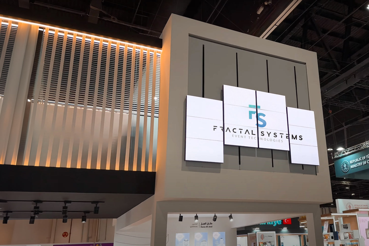 Fractal Systems' exhibition booth featuring their logo on a multi-panel digital display screen at a trade show.