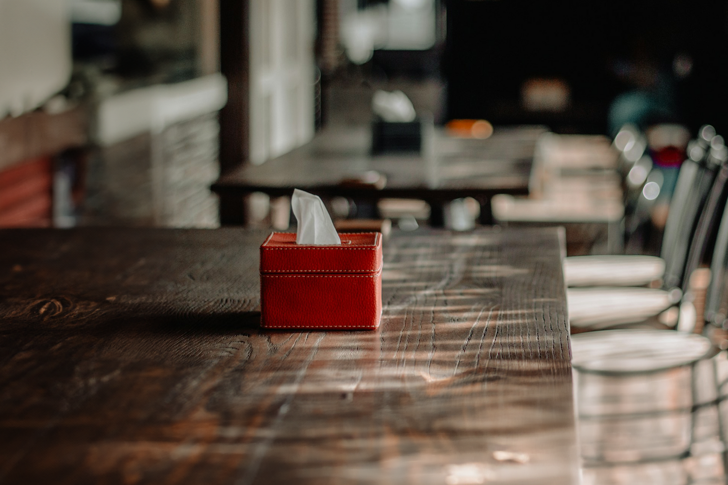 Red leather tissue holder on a wooden table in a restaurant setting, highlighting Trustline Enterprises' stylish and premium paper products for the foodservice industry.