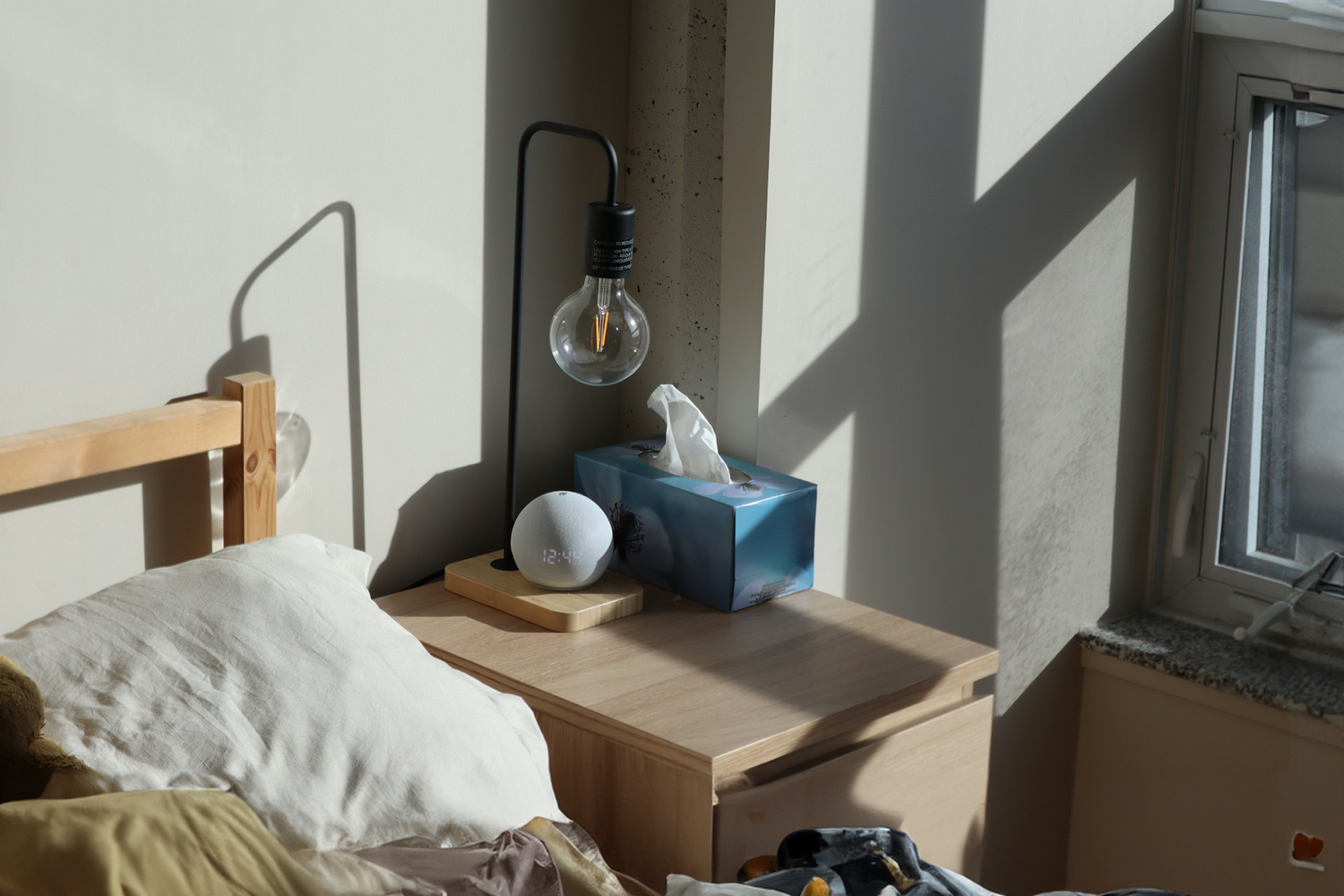 Bedside table with a box of tissues, lamp, and decor item in a sunlit room, demonstrating Trustline Enterprises' high-quality paper products for hospitality and healthcare settings.