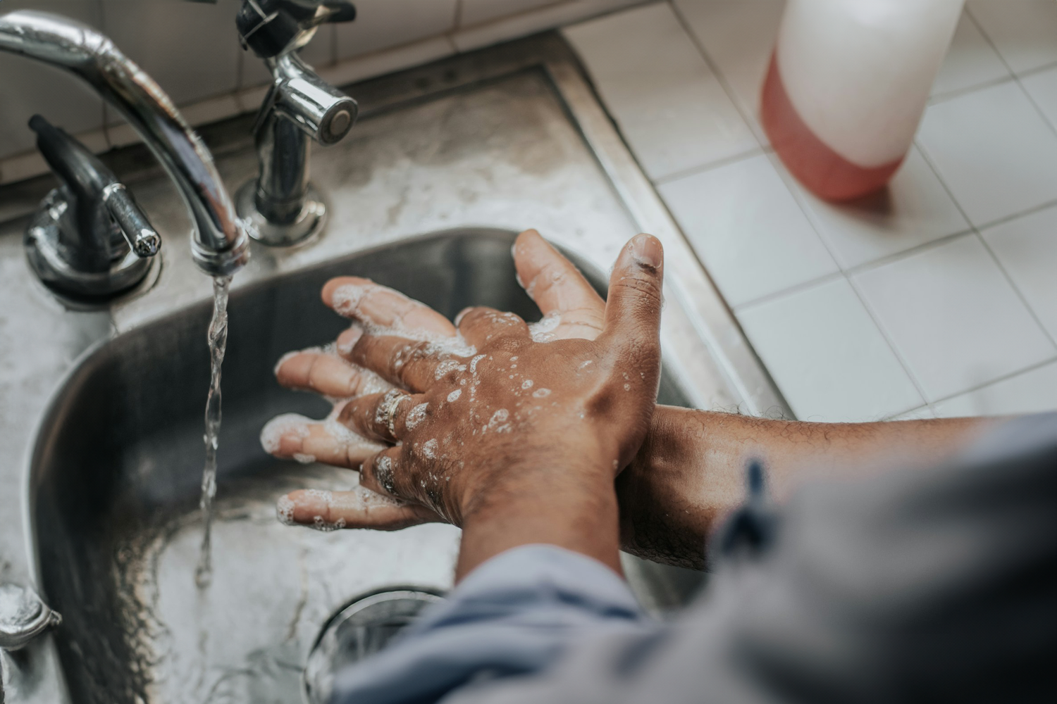 Person washing hands with soap at a sink, illustrating Trustline Enterprises' high-quality cleaning and hygiene supplies for healthcare and foodservice industries.