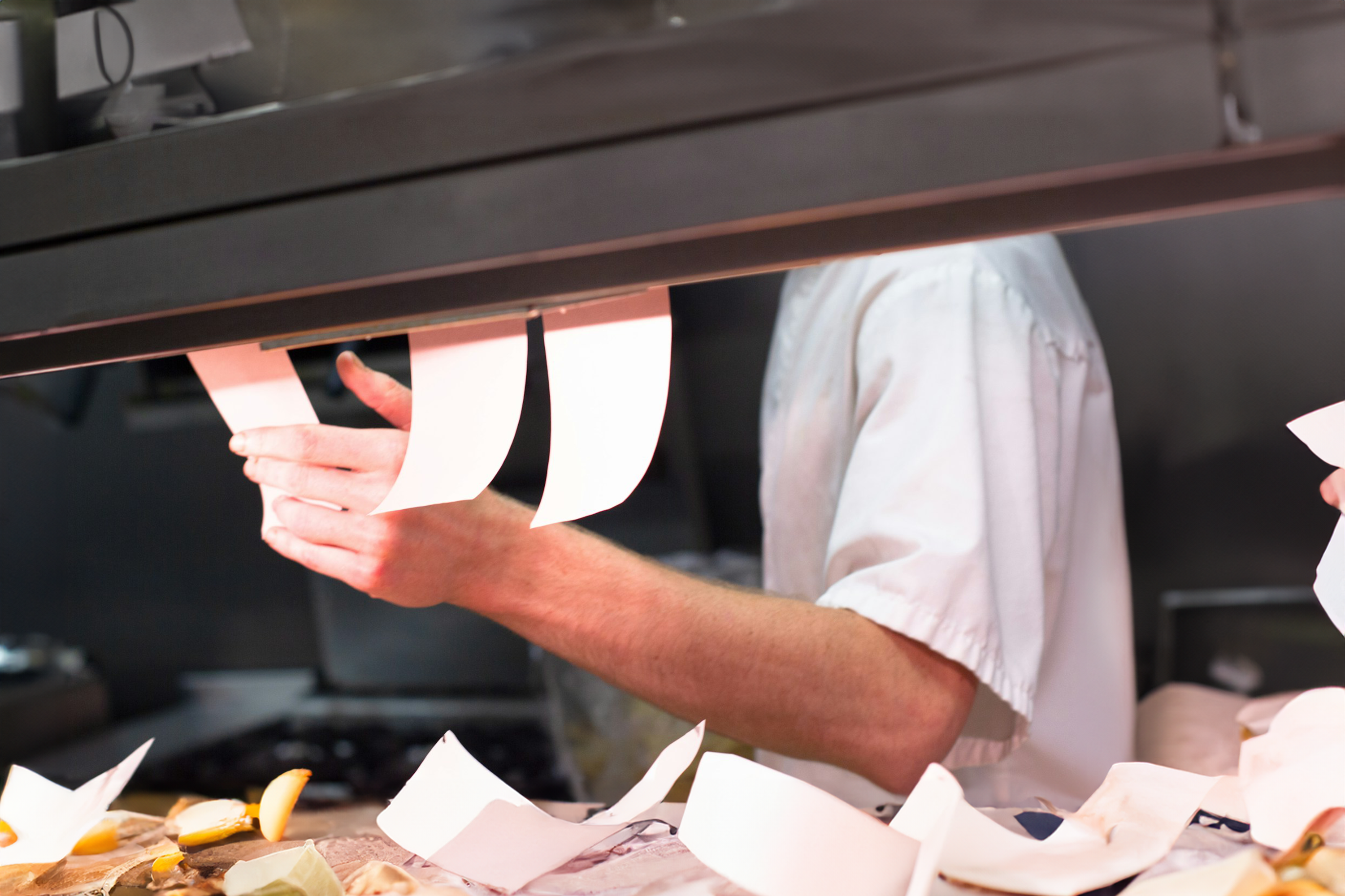 Chef in a commercial kitchen managing order tickets, emphasizing Trustline Enterprises' efficient and reliable supplies and solutions for the foodservice industry.