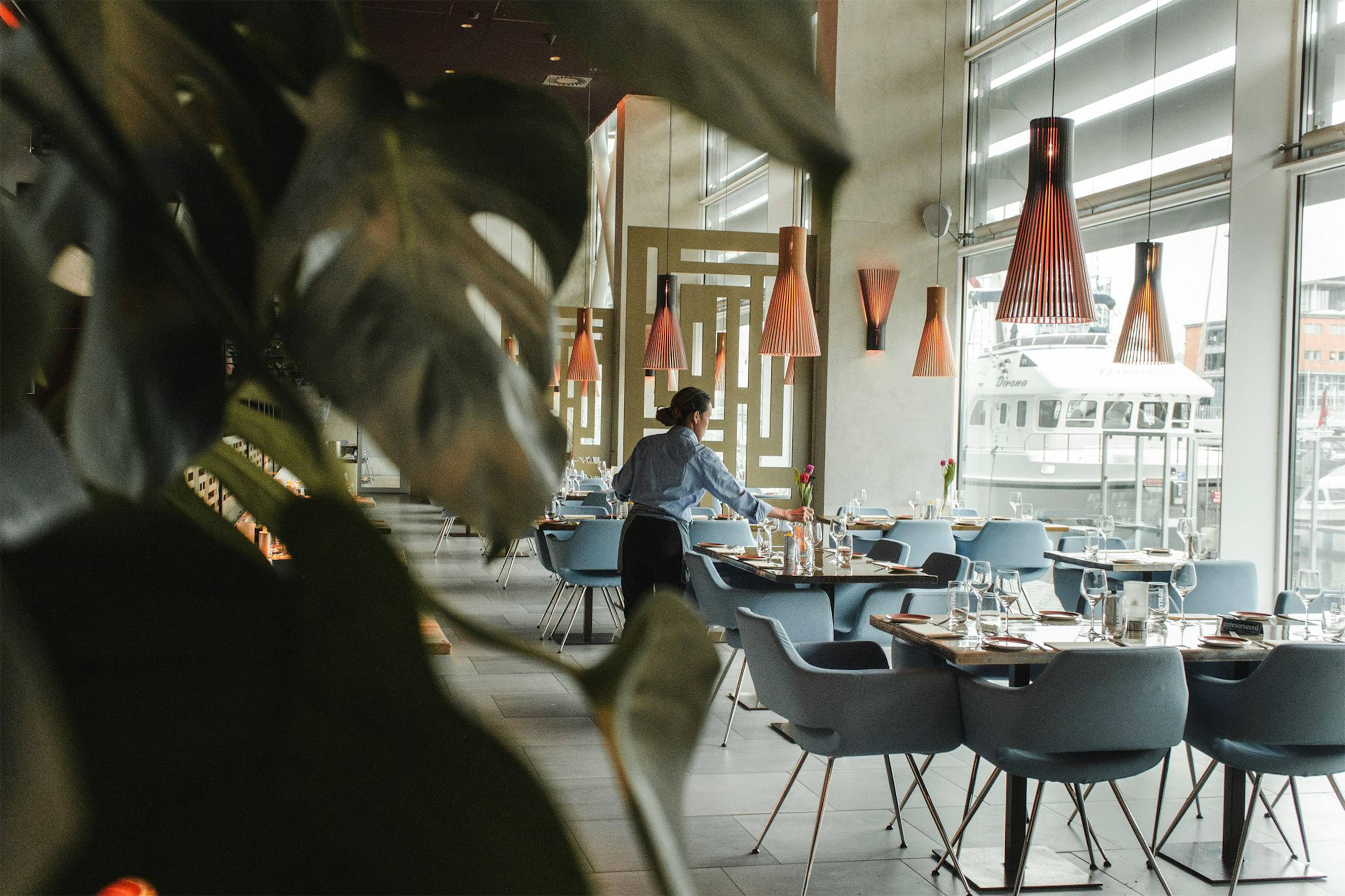 Restaurant interior with a server setting tables, showcasing Trustline Enterprises' products and services for the hospitality industry, including tableware, cleaning supplies, and uniform solutions.