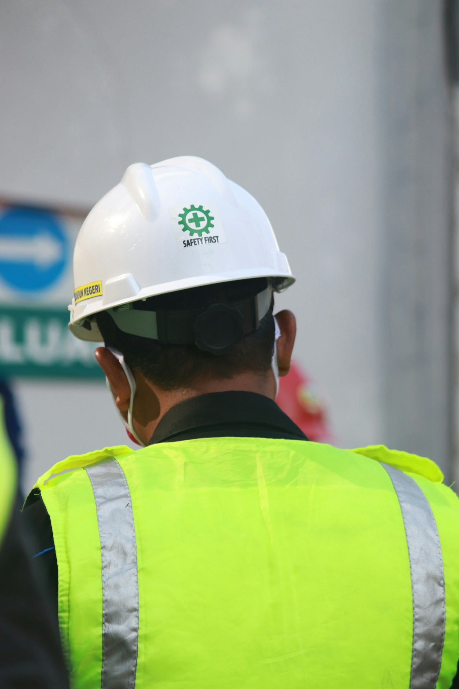 Construction worker wearing a safety helmet and high-visibility vest by Trustline Enterprises, viewed from behind.