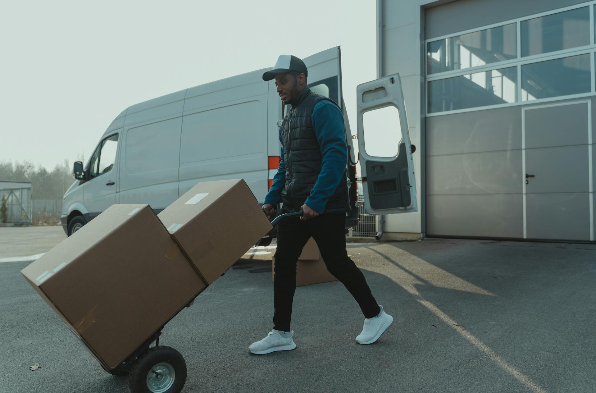 A delivery worker moving boxes with a hand truck near a van.