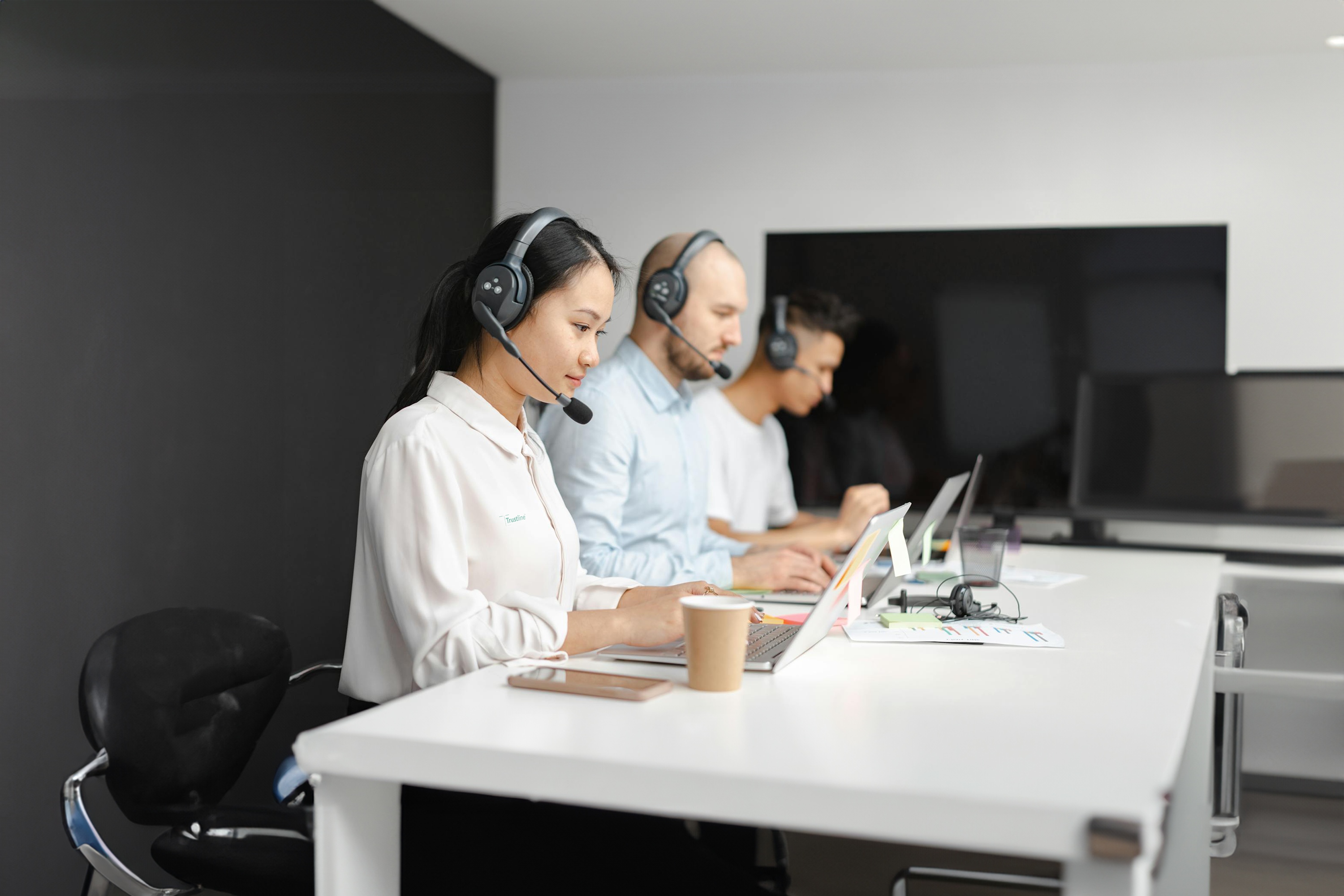 Three customer service representatives with headsets working on laptops in an office setting, focusing on their tasks.