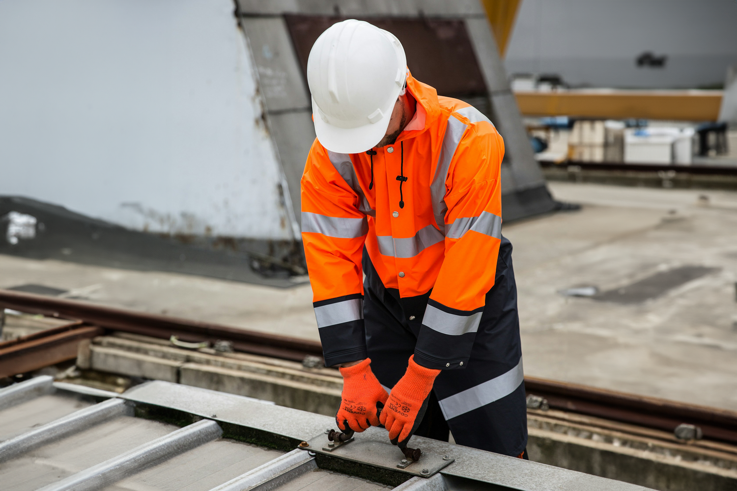 Construction worker wearing a high-visibility uniform and safety gear by Trustline Enterprises, securing equipment on a rooftop.