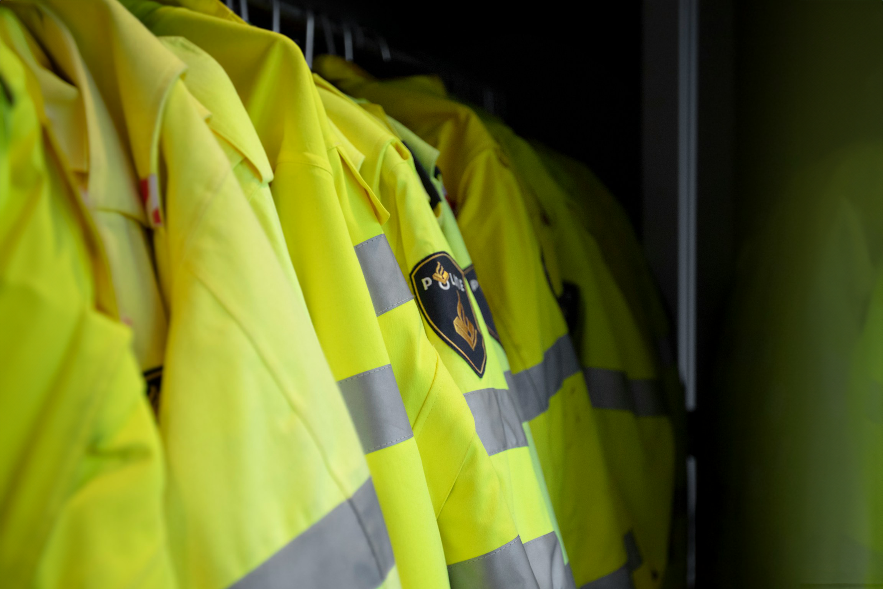 Close-up of high-visibility police jackets hanging in a row, featuring reflective stripes and a police emblem patch.